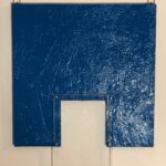 A blue-painted board or panel mounted on a wall with two metal hanging hooks. In the center, there's a clear acrylic or plastic rectangular frame mounted to the blue surface. The blue paint shows a textured, distressed appearance. Latex and plexiglass on chipboard, 14″ x 12, 2024 by James K-M