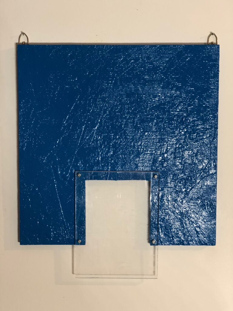 A blue-painted board or panel mounted on a wall with two metal hanging hooks. In the center, there's a clear acrylic or plastic rectangular frame mounted to the blue surface. The blue paint shows a textured, distressed appearance. Latex and plexiglass on chipboard, 14″ x 12, 2024 by James K-M